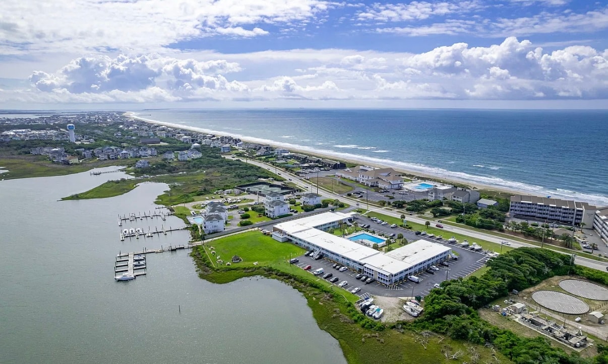 Sweeping aerial view of Atlantic Beach NC barrier island showing Bogue Sound on the left, the Atlantic Ocean on the right, marina, and coastal development stretching to the horizon