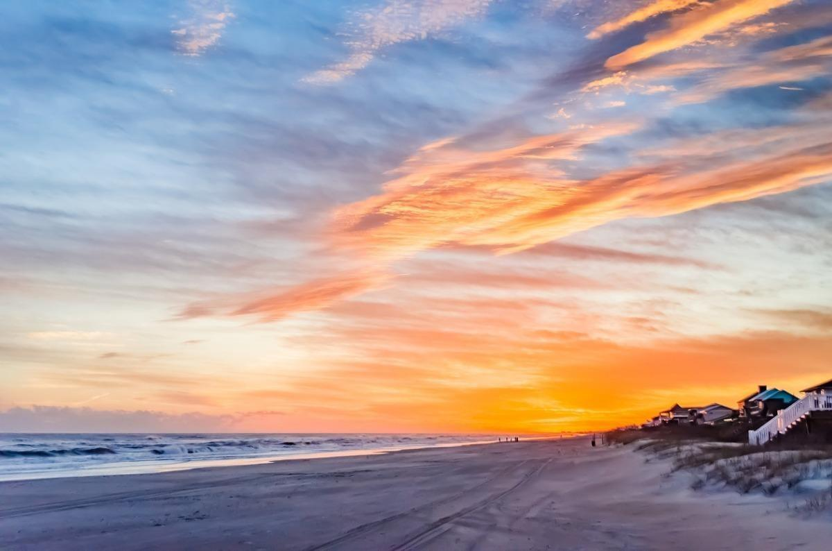 Dramatic Atlantic Beach NC sunset with blazing orange and pink sky over the ocean and beach houses along the shore