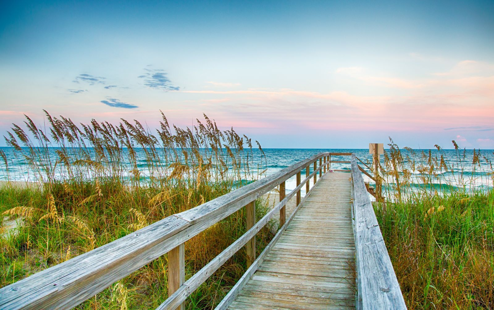 Wooden boardwalk through sea oats and coastal dunes leading to the Atlantic Beach NC shoreline at sunset
