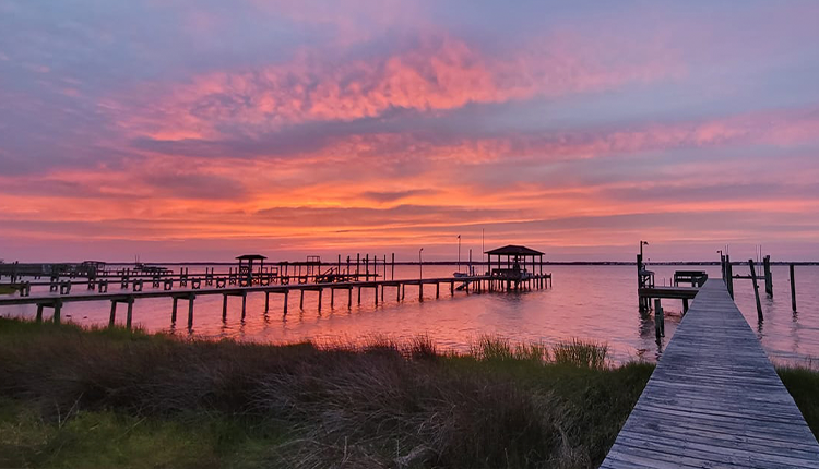 Blazing pink and purple sunset over Bogue Sound with wooden piers and boat docks silhouetted against the sky Atlantic Beach NC