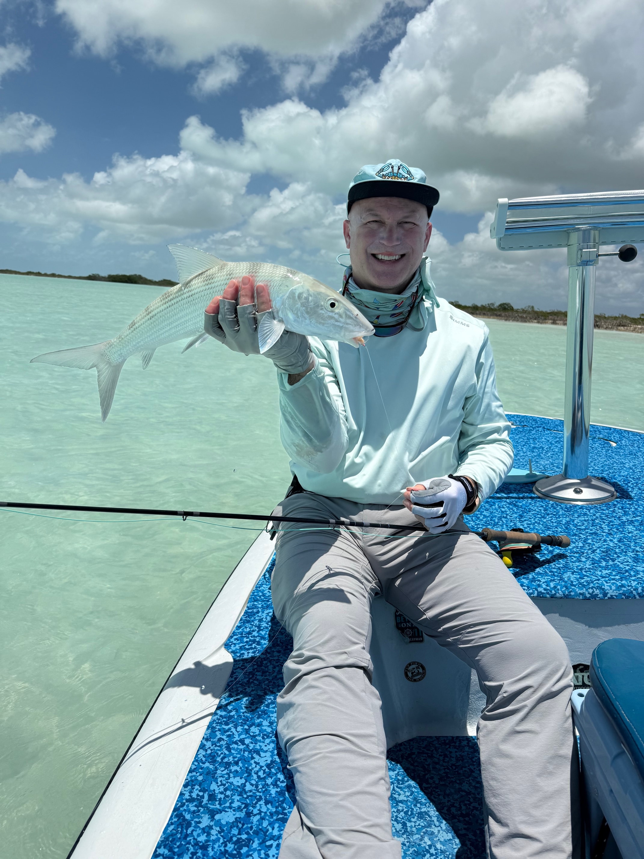 Angler on flats boat holding a bonefish with turquoise Andros water and clouds behind